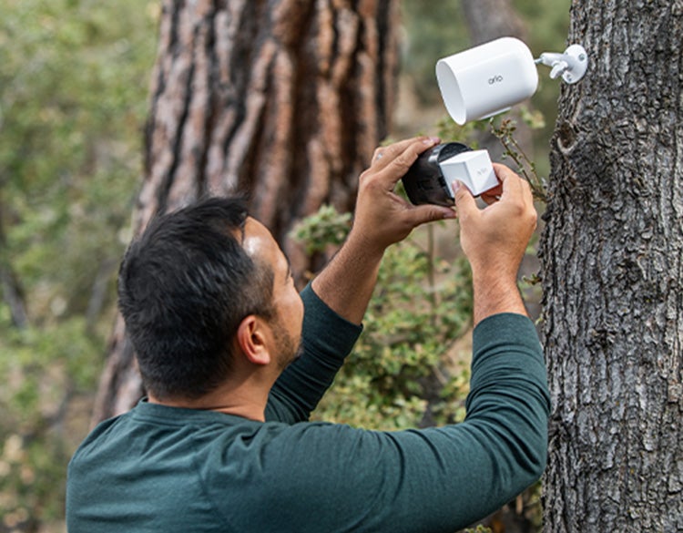 Un homme installe la caméra mobile Arlo Go 2 contre un arbre