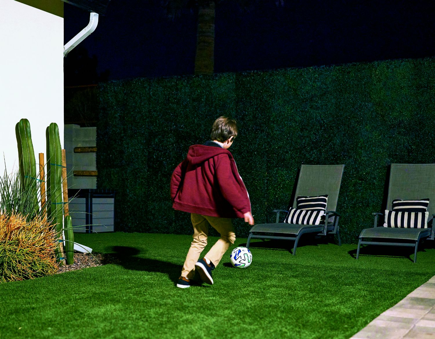 A young boy in the garden at night plays football in the garden