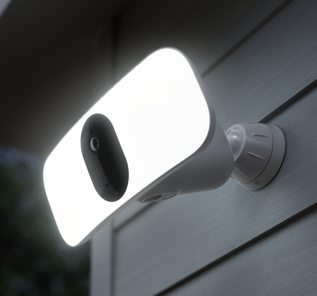 The Arlo Floodlight, an outdoor security camera with a powerful built-in spotlight, installed against a wall at night, illuminates the surroundings with the power of the spotlight. 